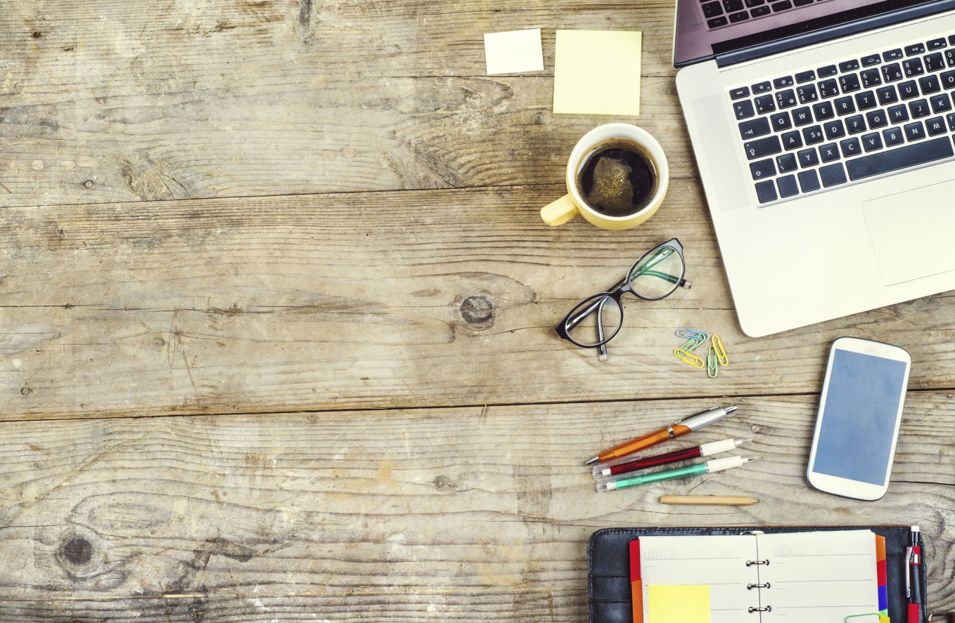 Mix of office supplies and gadgets on a wooden table background. View from above.